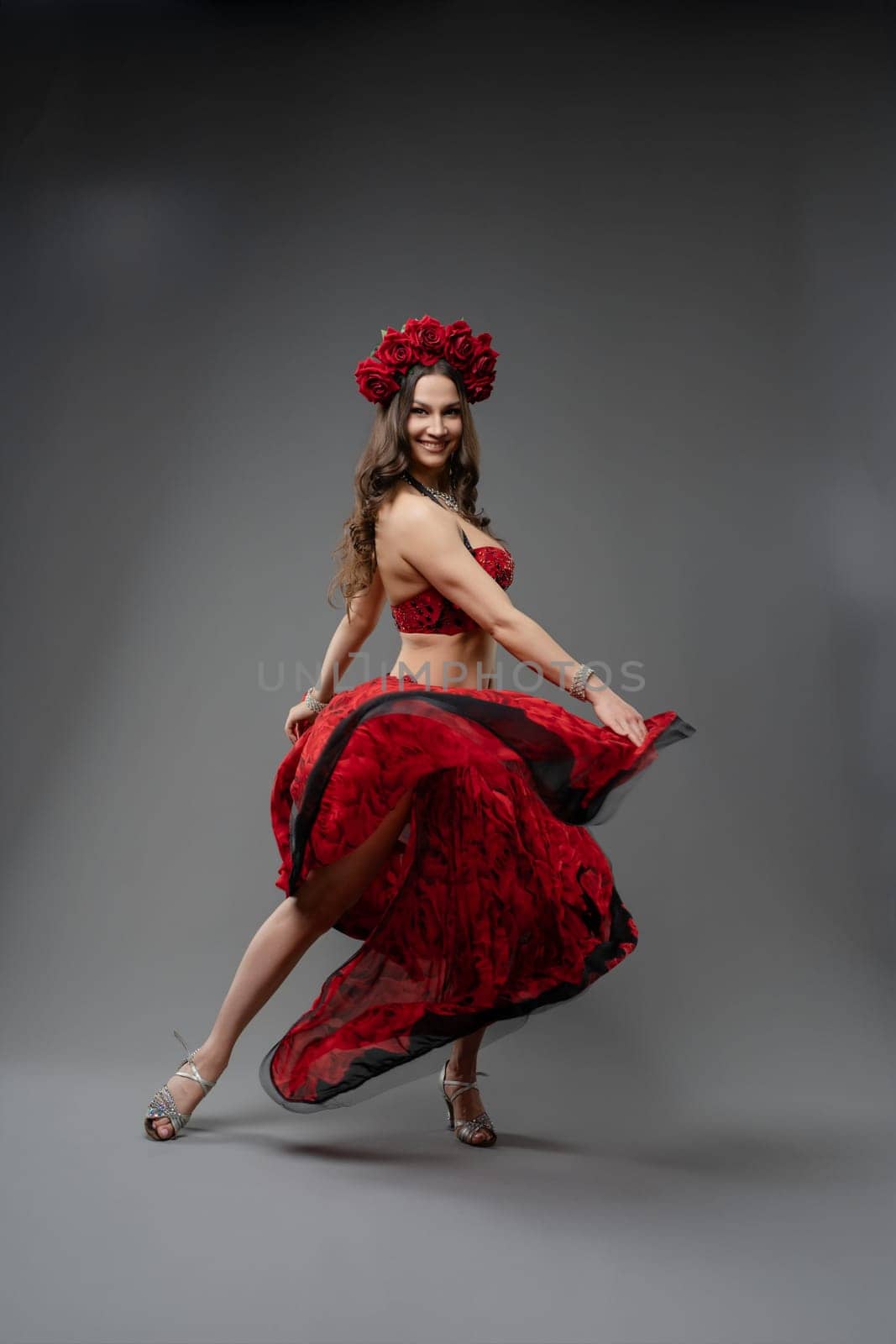 A dancer showcases her skills in a stunning red dress, spinning elegantly under studio lights. Her floral headpiece adds to the festive ambiance.