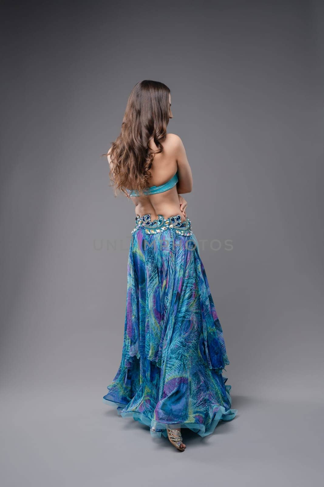 A dancer gracefully turns, displaying a flowing blue skirt and intricate details, emphasizing movement and elegance in a studio environment.