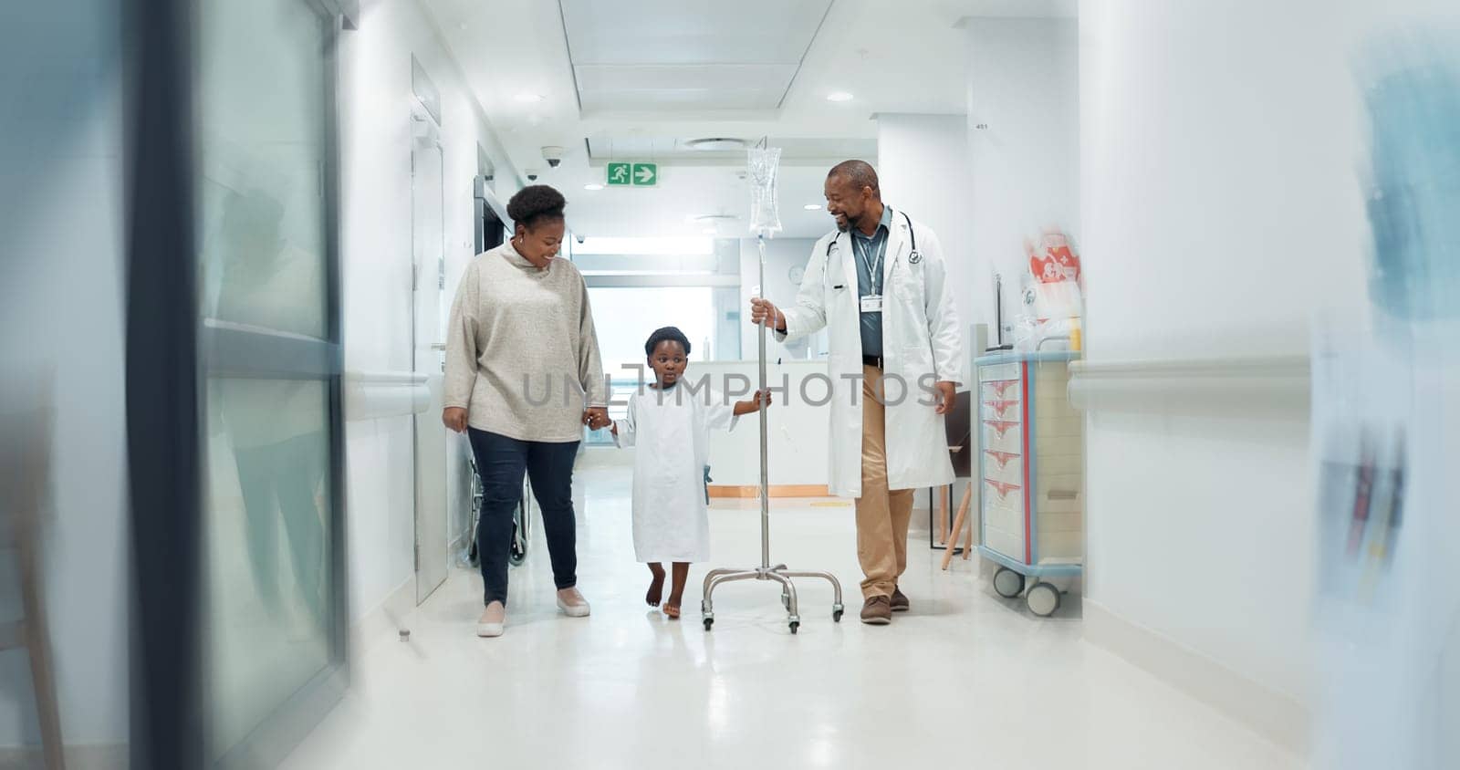 Medical, pediatrician and a doctor walking with a black family in a hospital corridor for diagnosis. Healthcare, communication and consulting with a medicine professional talking to a boy patient by YuriArcurs