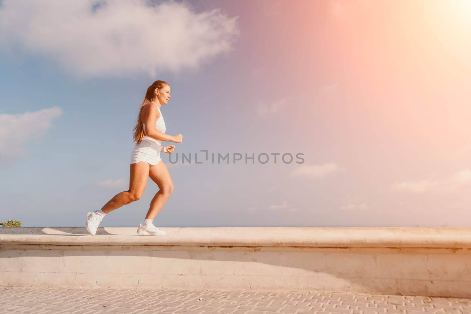 Fitness woman sea. Active, happy middle-aged woman in white sportswear exercises outdoors in a park over sea. Healthy lifestyle, physical activity and female fitness pilates and yoga routines. by panophotograph