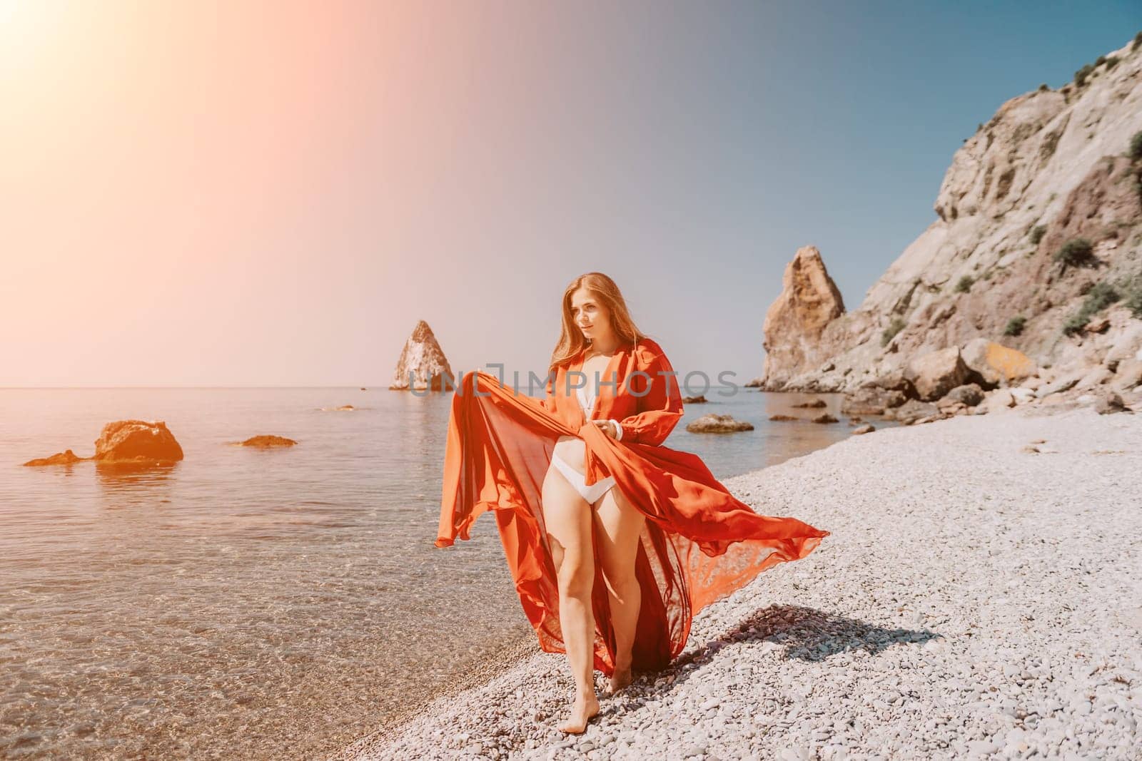 Woman travel sea. Happy tourist in red dress enjoy taking picture outdoors for memories. Woman traveler posing on the rock at sea bay surrounded by volcanic mountains, sharing travel adventure journey by panophotograph