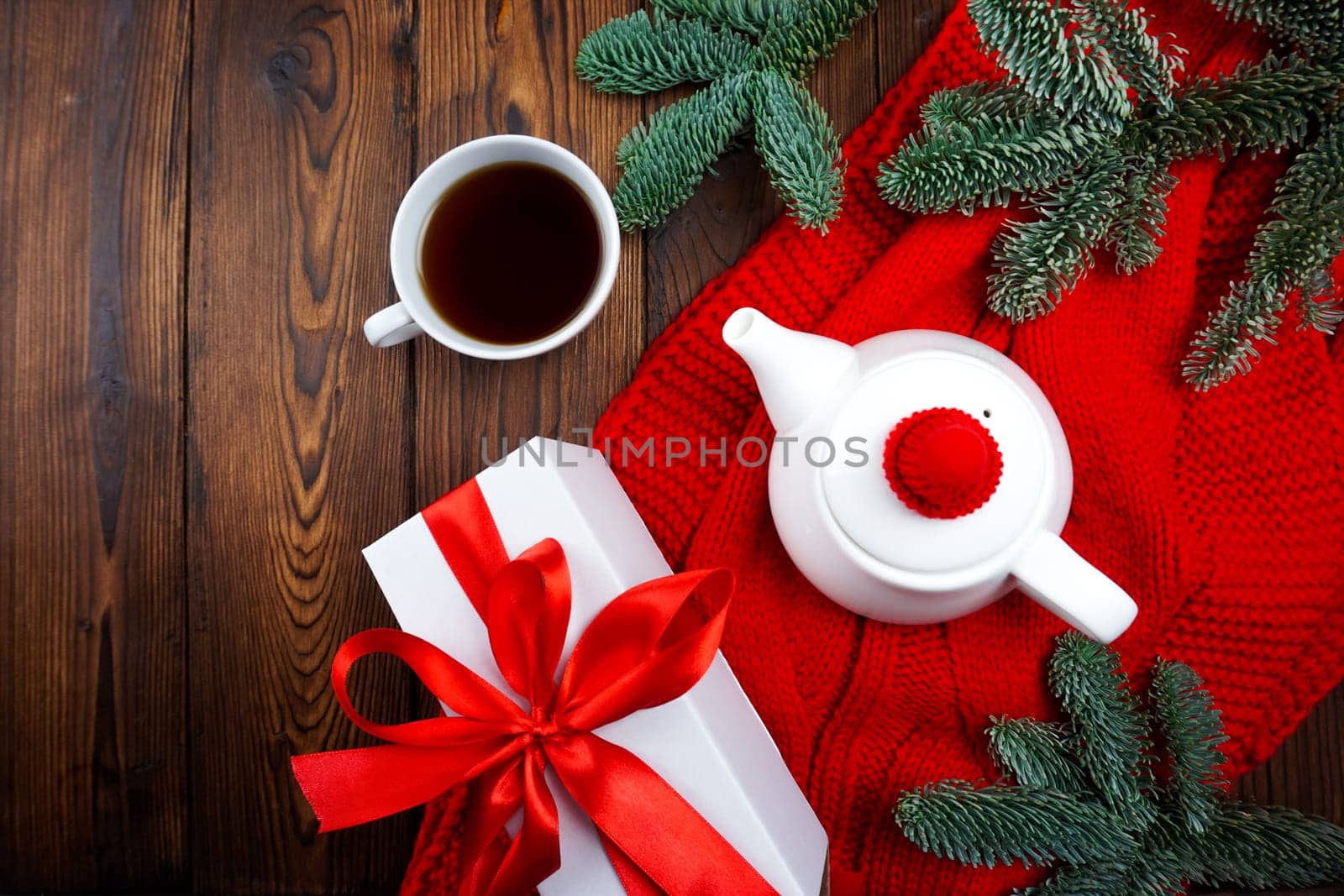 On a wooden background there is a red scarf and there is a teapot and a cup of tea by Spirina