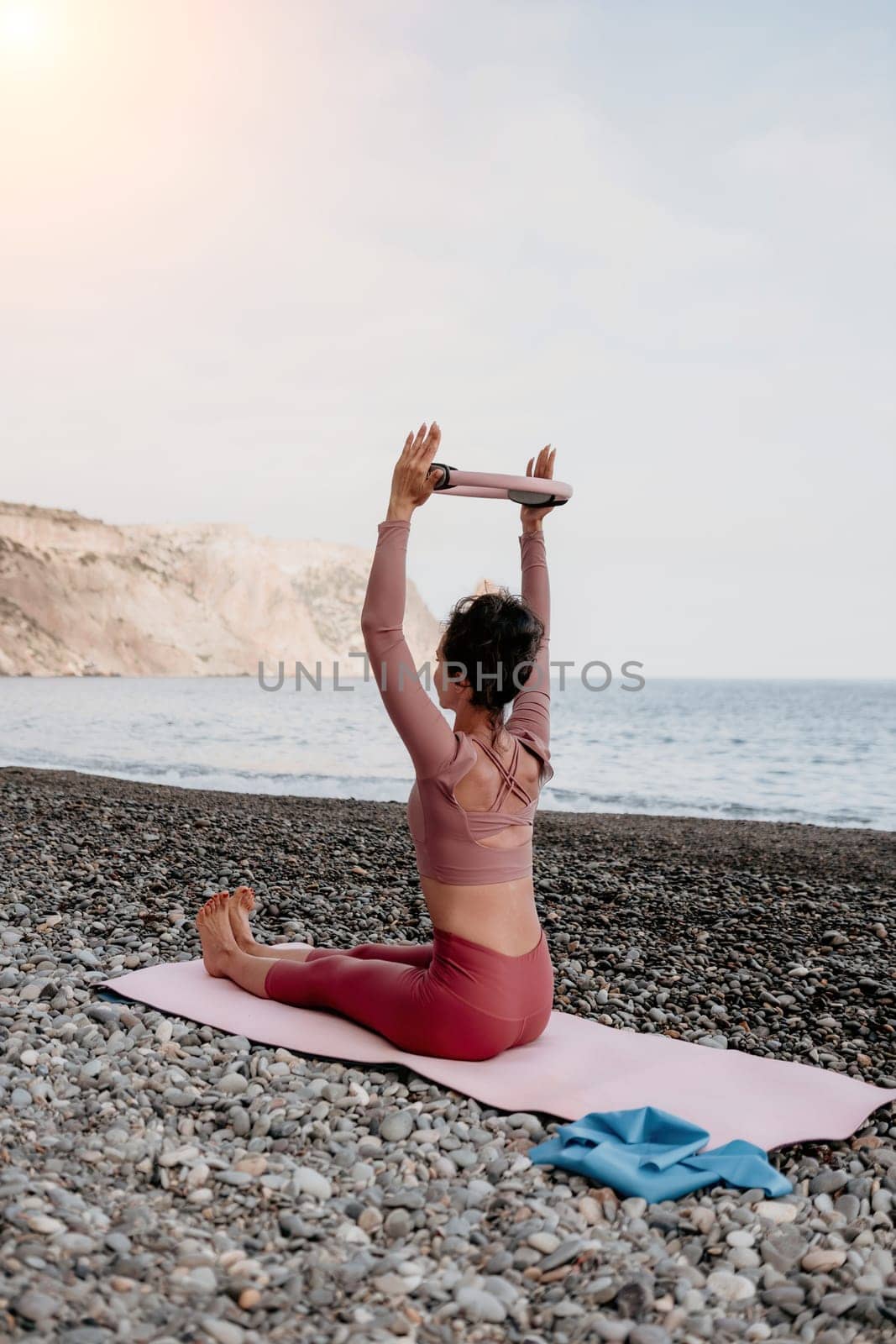 Woman sea pilates. Sporty happy middle aged woman practicing fitness on beach near sea, smiling active female training with ring on yoga mat outside, enjoying healthy lifestyle, harmony and meditation by panophotograph