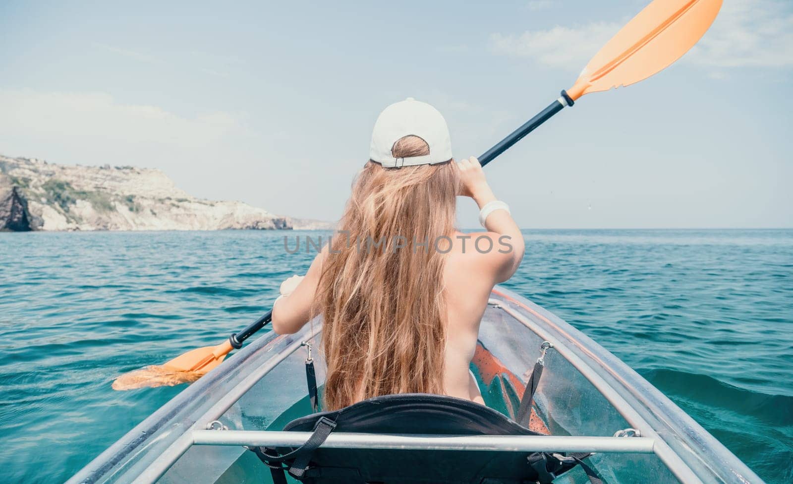 Woman in kayak back view. Happy young woman with long hair floating in transparent kayak on the crystal clear sea. Summer holiday vacation and cheerful female people relaxing having fun on the boat by panophotograph