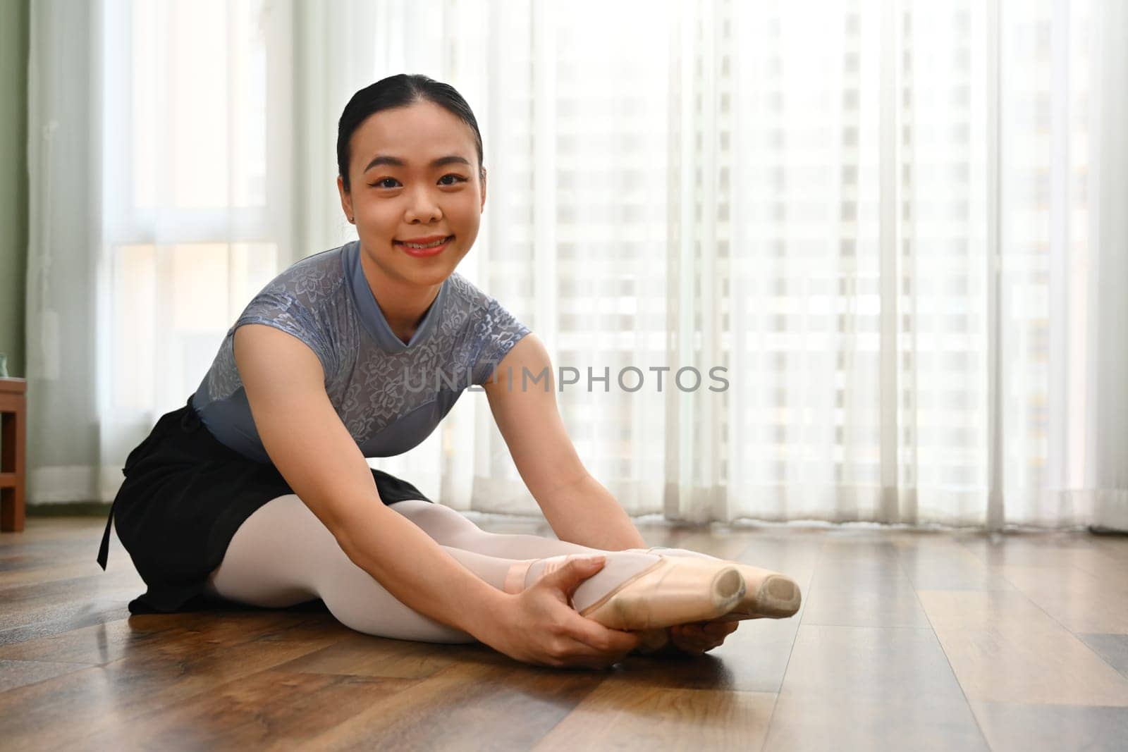 Beautiful ballerina sitting on the floor, warming up before dance class. Dance, art and flexibility concept.