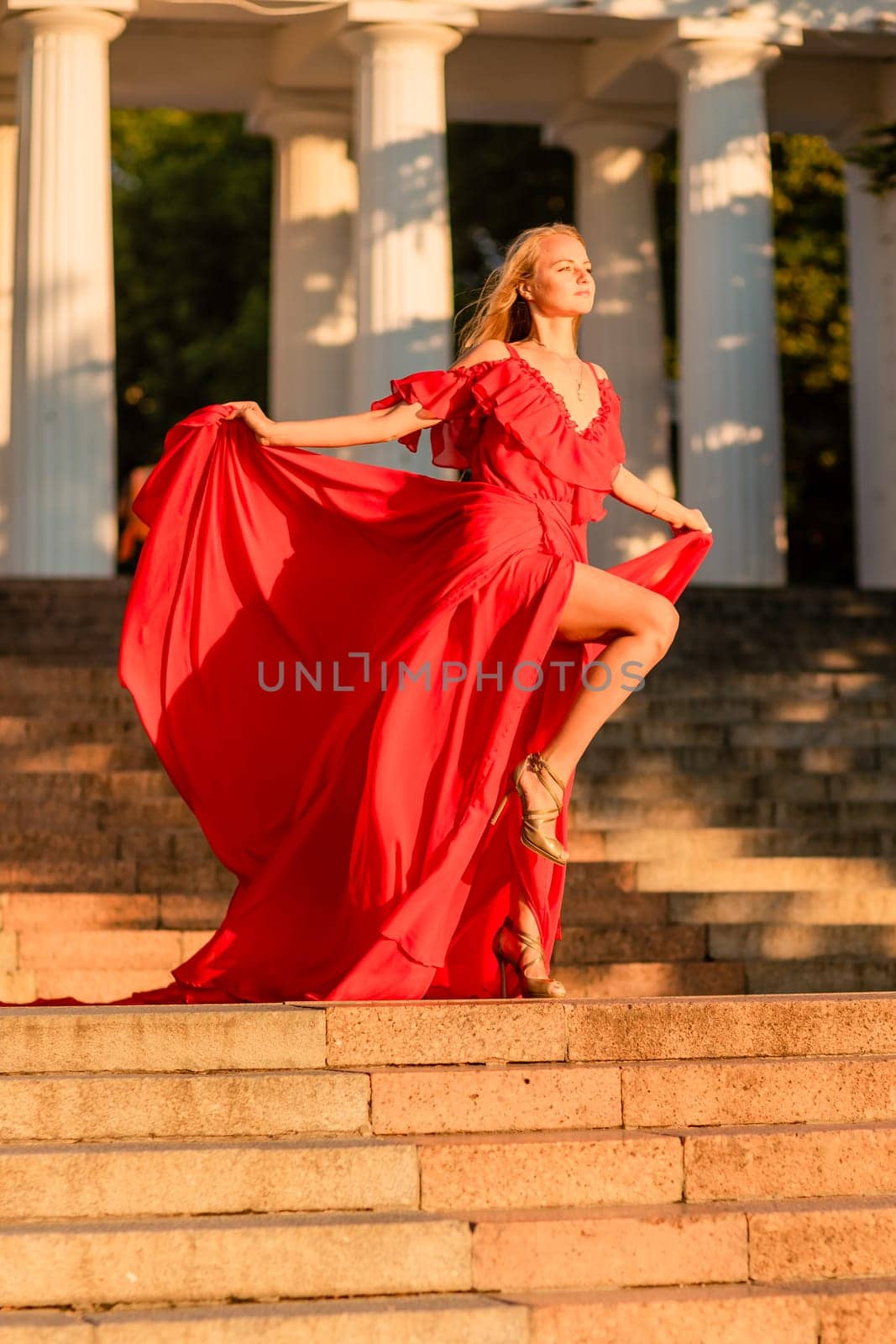 A woman in a long red dress against the backdrop of sunrise, bright golden light of the sun's rays. The concept of femininity, harmony. by Matiunina