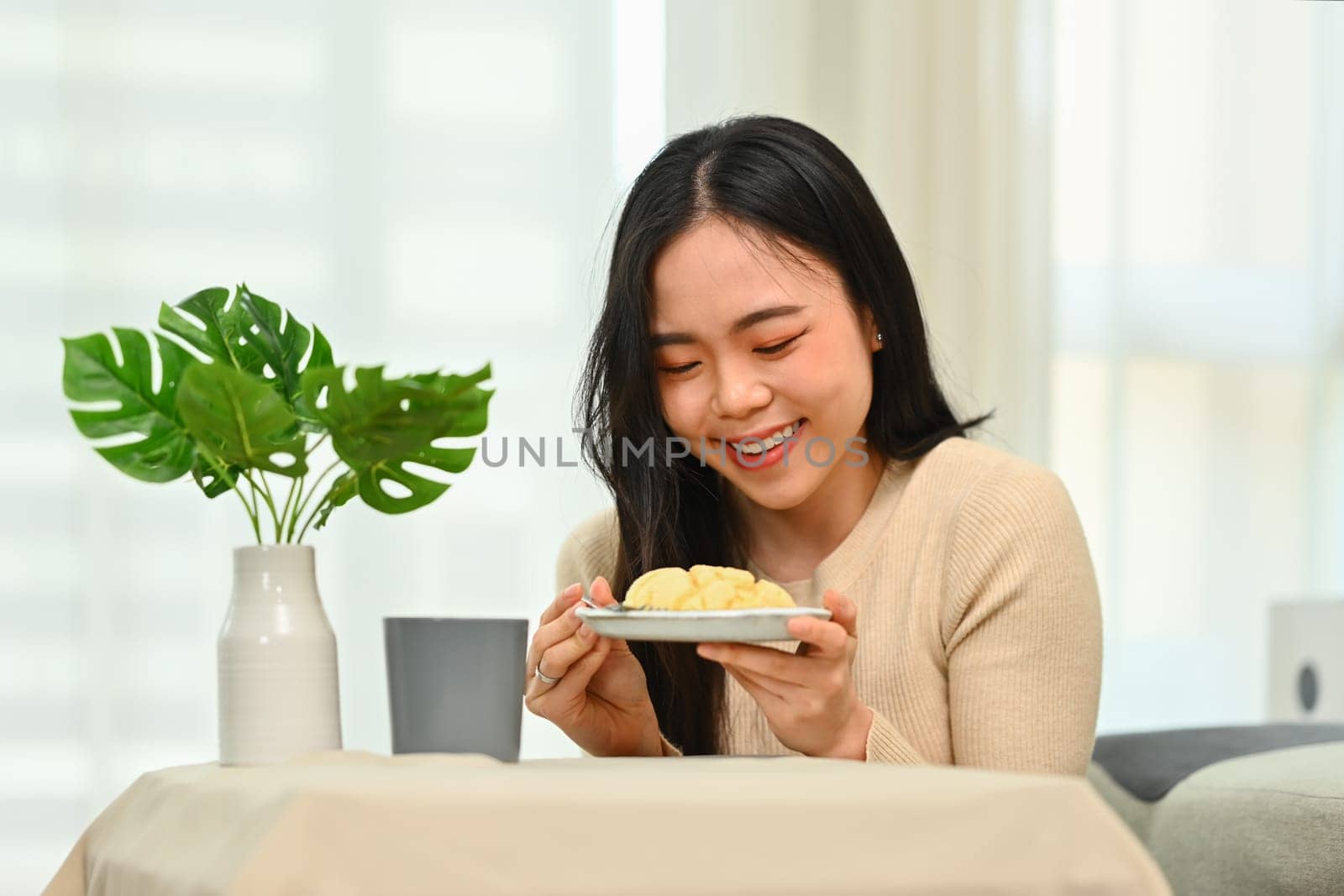 Cheerful young asian woman in casual clothes having breakfast at home. Concept of wellness, food and domestic lifestyle by prathanchorruangsak