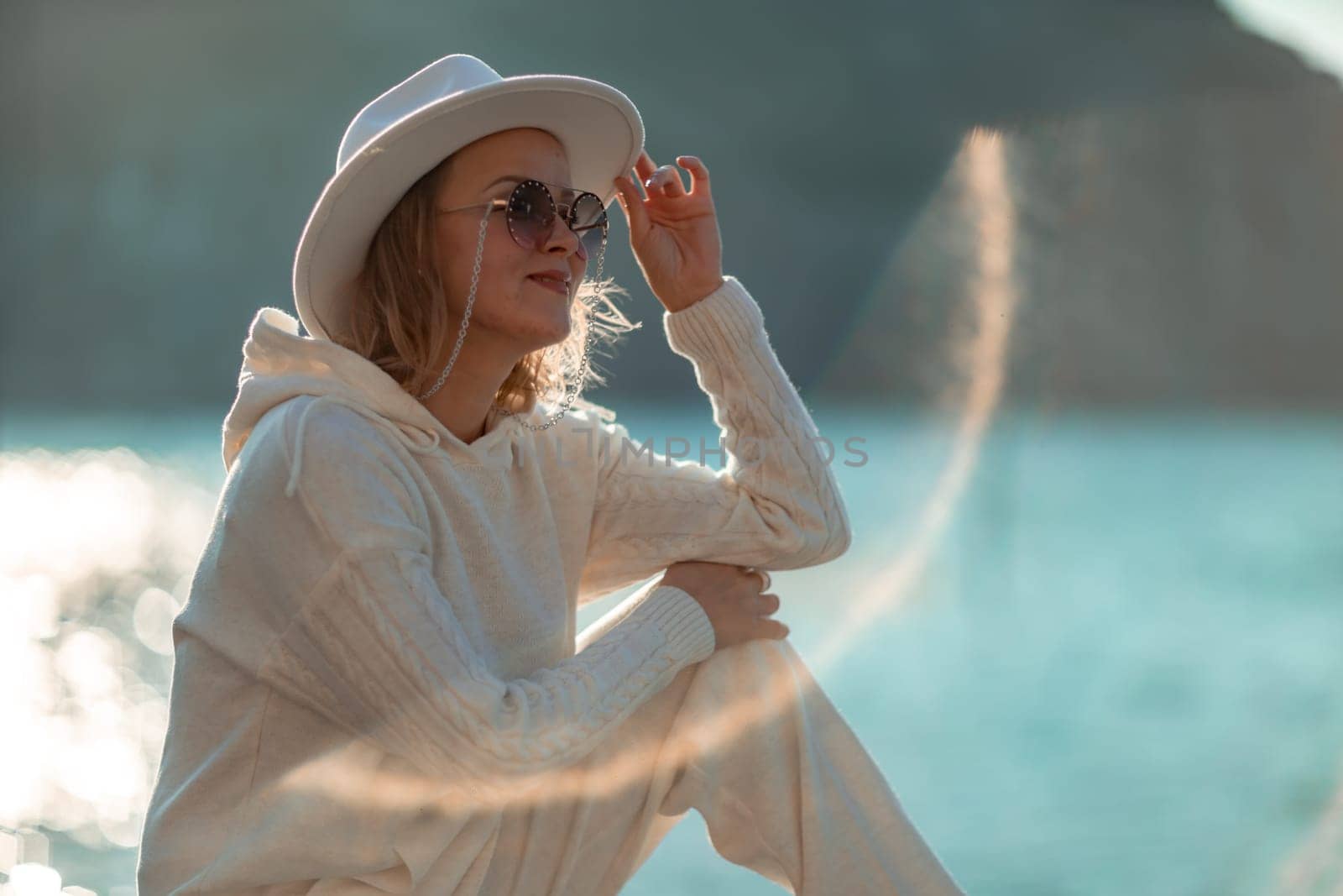 Happy blonde woman in a white suit and hat posing at the camera against the backdrop of the sea by Matiunina