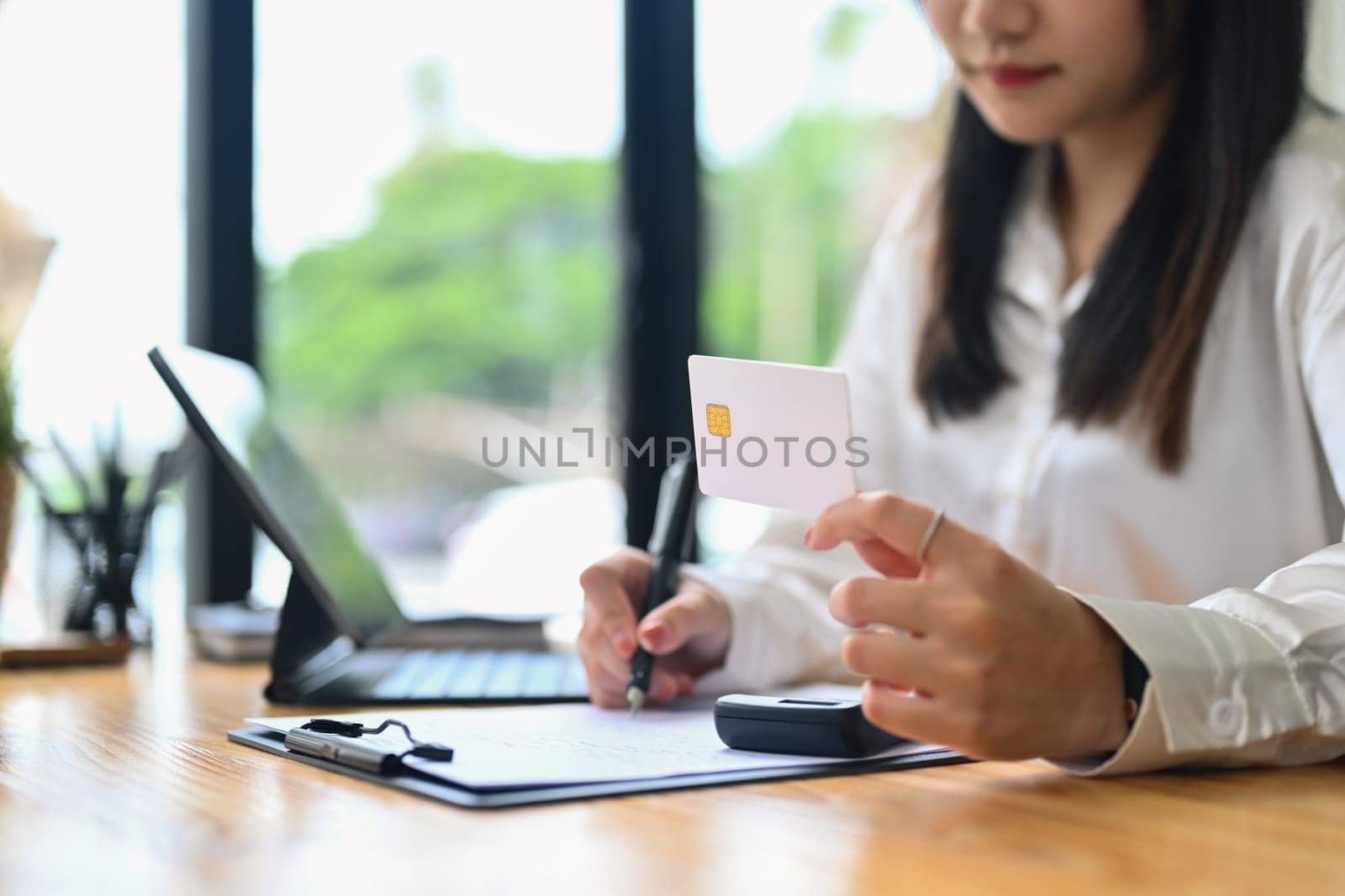 Select focus on woman hand holding credit card and writing notes. Electronic money, contactless payment concept.