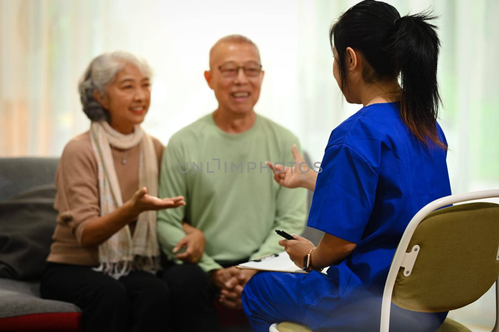 Attentive doctor or healthcare worker giving professional advice to senior couple during home visit. Elderly and healthcare concept by prathanchorruangsak