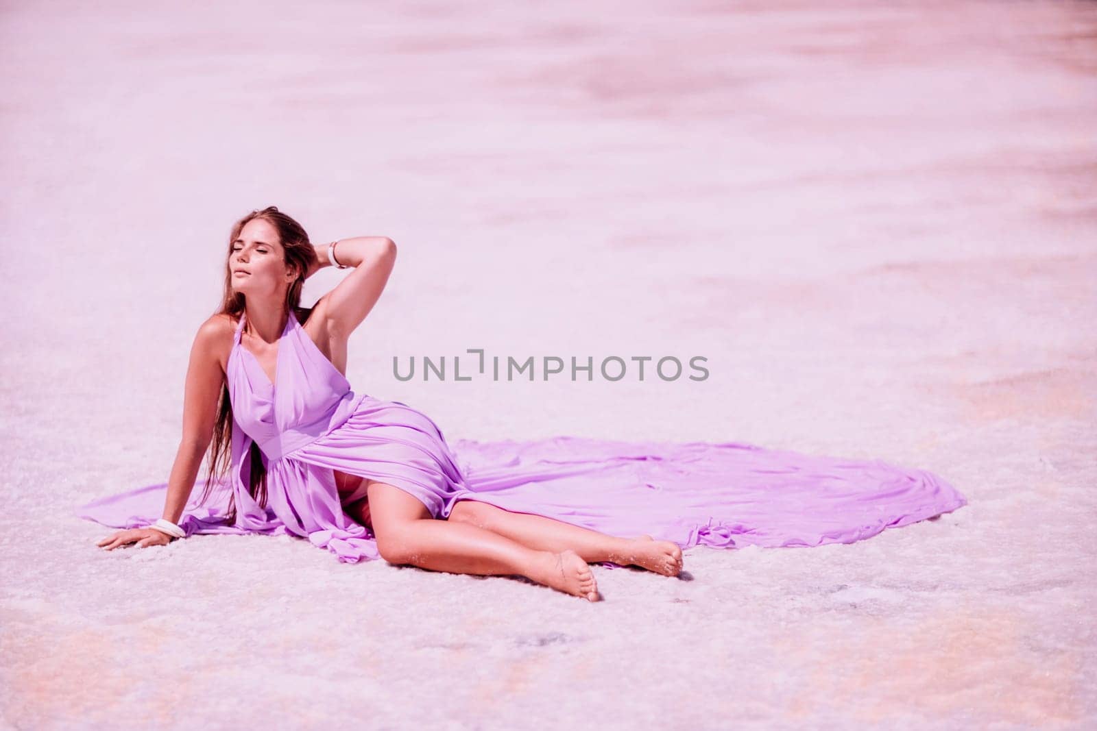 A woman in a pink dress sits on the salty shore of a pink lake and poses for a souvenir photo, creating lasting memories. by Matiunina