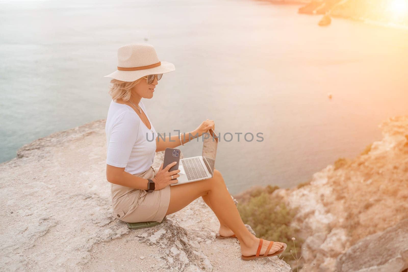 Freelance women sea working on the computer. Good looking middle aged woman typing on a laptop keyboard outdoors with a beautiful sea view. The concept of remote work