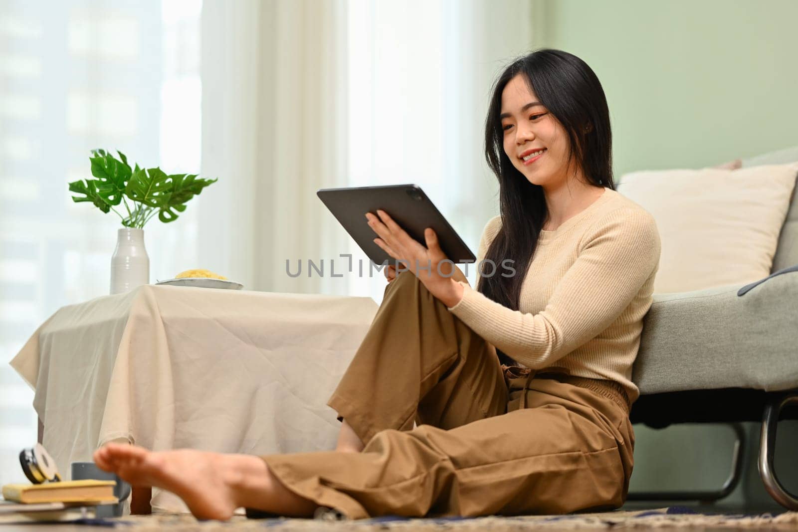 Charming young woman using digital tablet while sitting on floor in living room. Technology and lifestyle concept.