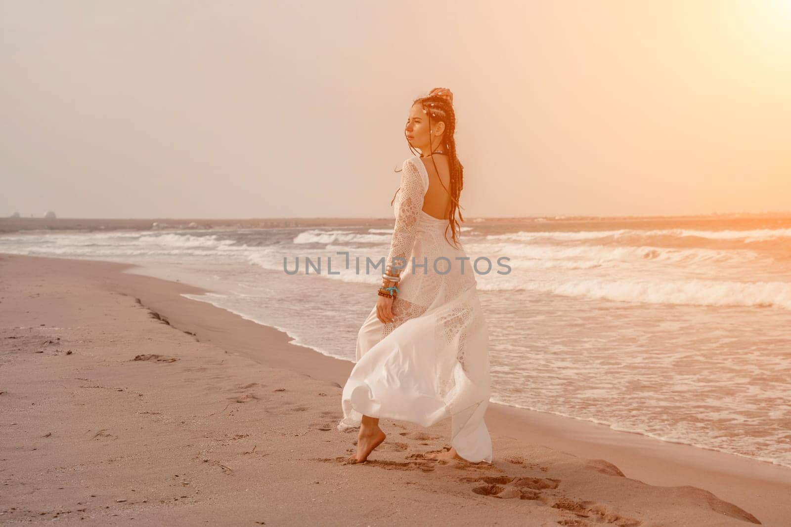 woman sea white dress. Model in boho style in a white long dress and silver jewelry on the beach. Her hair is braided, and there are many bracelets on her arms. by Matiunina