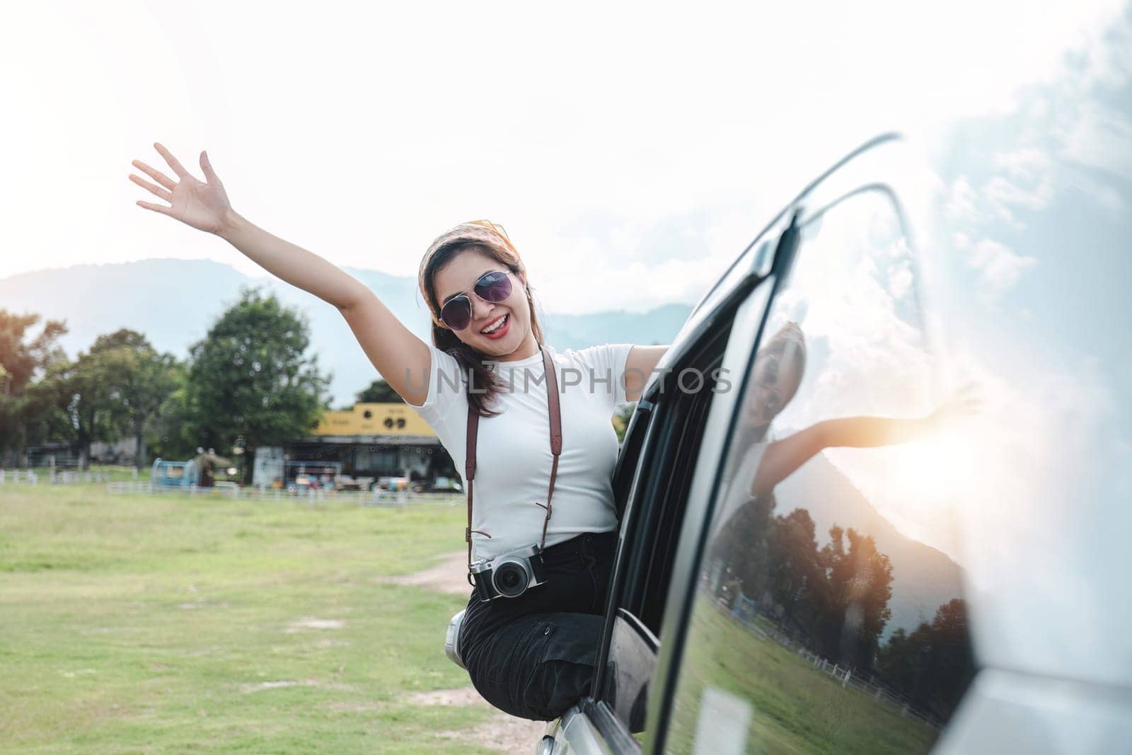 Happy young Asian woman enjoying a road trip and having fun waving at the air outside the car. by wichayada