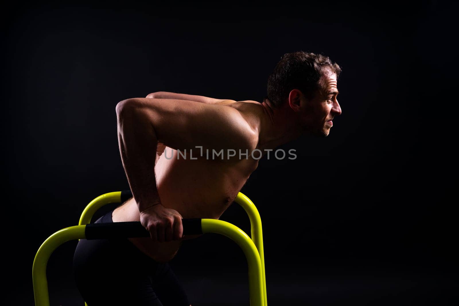 Front and side view photo of strong young man exercising on parallel bars in studio.