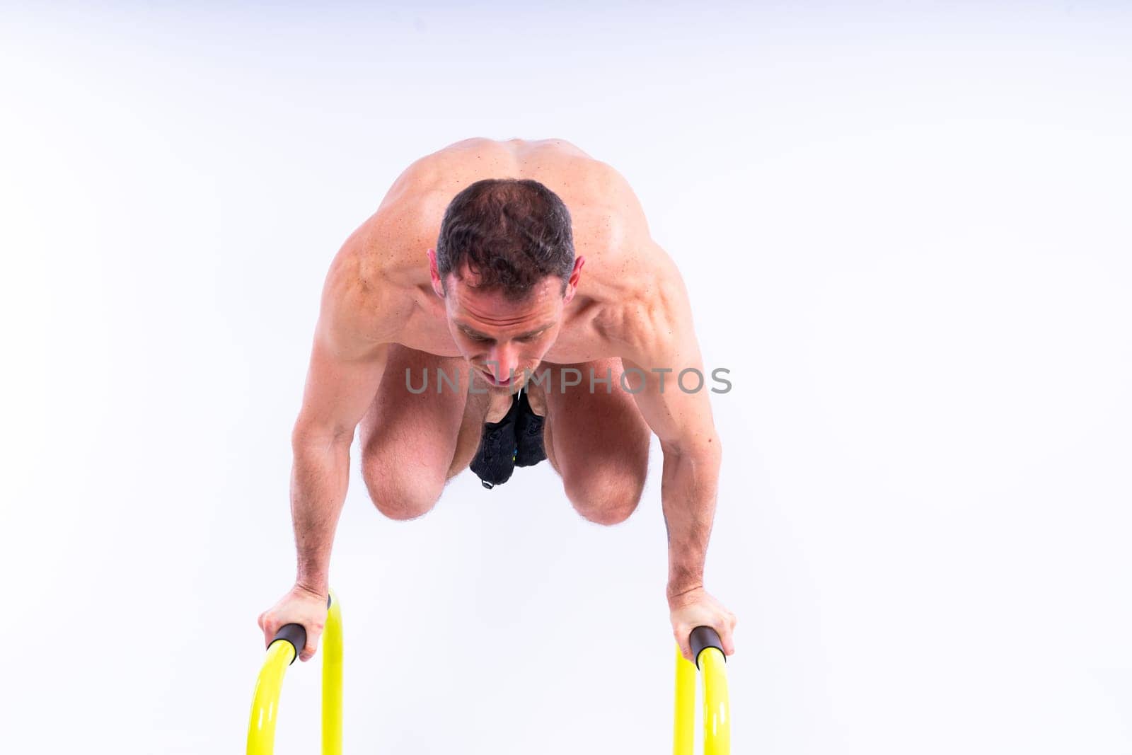 Front and side view photo of strong young man exercising on parallel bars in studio.