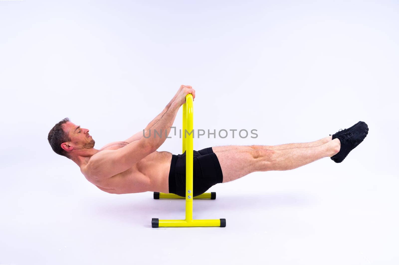 Front and side view photo of strong young man exercising on parallel bars in studio.
