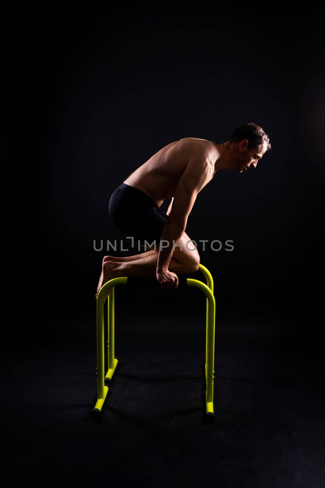 Front and side view photo of strong young man exercising on parallel bars in studio.