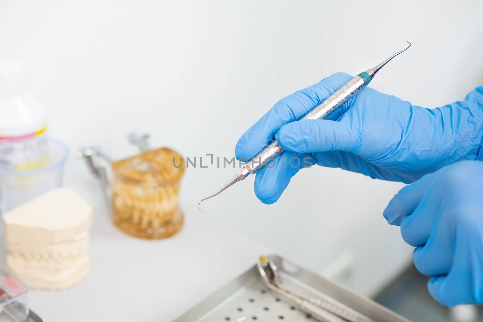 A dentist's hands holding dental instruments for teeth treatment, with jaw models in the background.