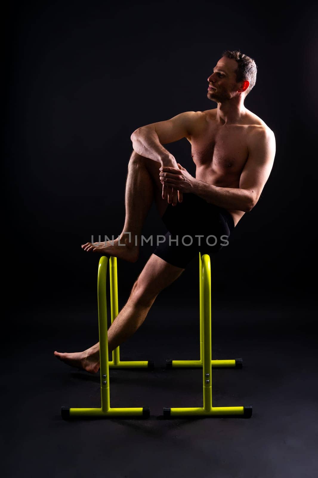 Front and side view photo of strong young man exercising on parallel bars in studio.