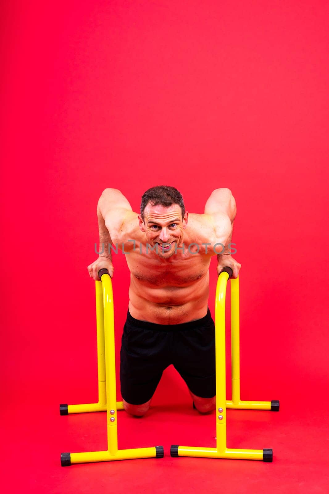 Front and side view photo of strong young man exercising on parallel bars in studio.