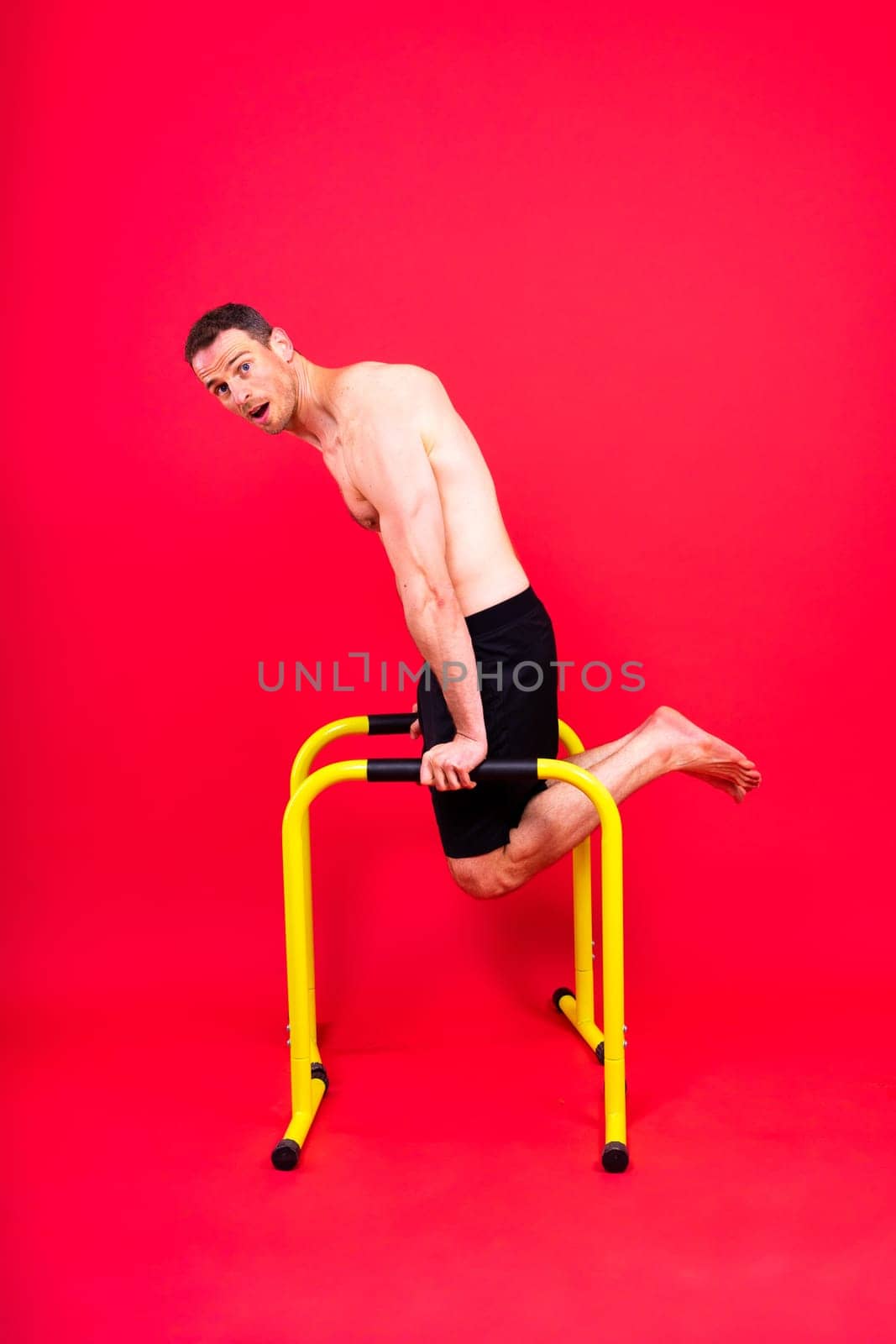 Front and side view photo of strong young man exercising on parallel bars in studio.