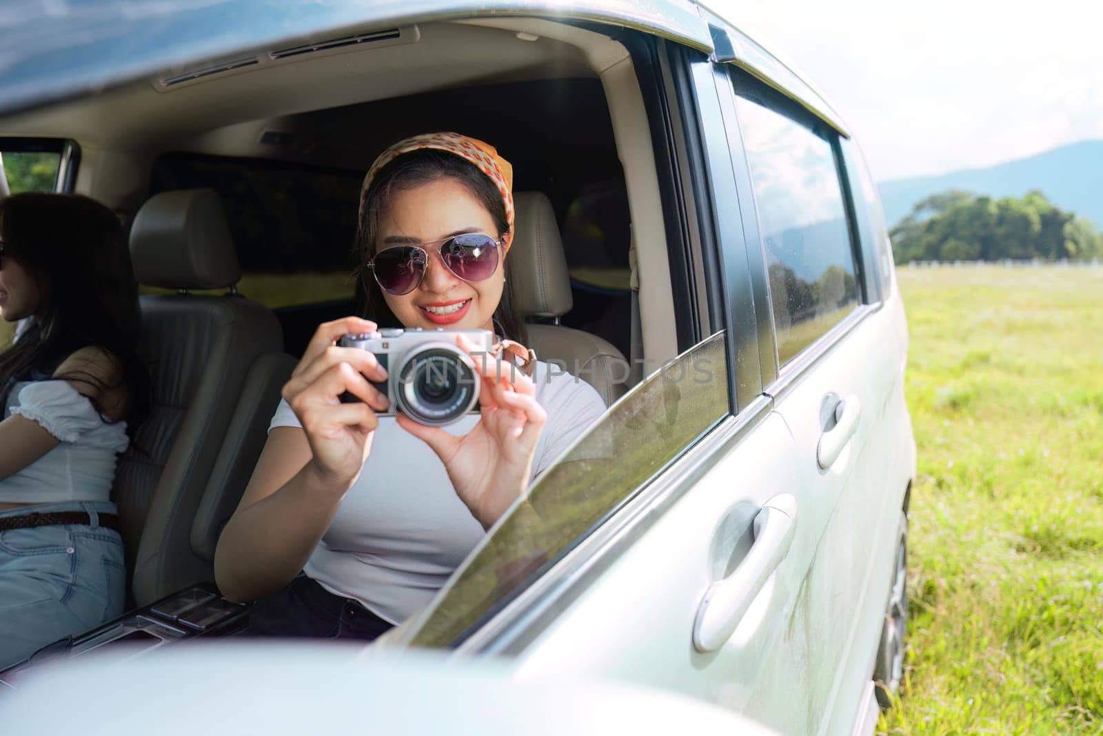 beautiful female smiling friends going on a trip while sticking head out of car in motion to see the view and take photos.
