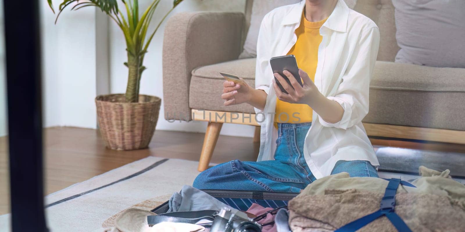 Young traveler woman using smartphone to book a hotel and search for tourist attraction information while prepare travel suitcase before going on summer vacation. Online booking concept.