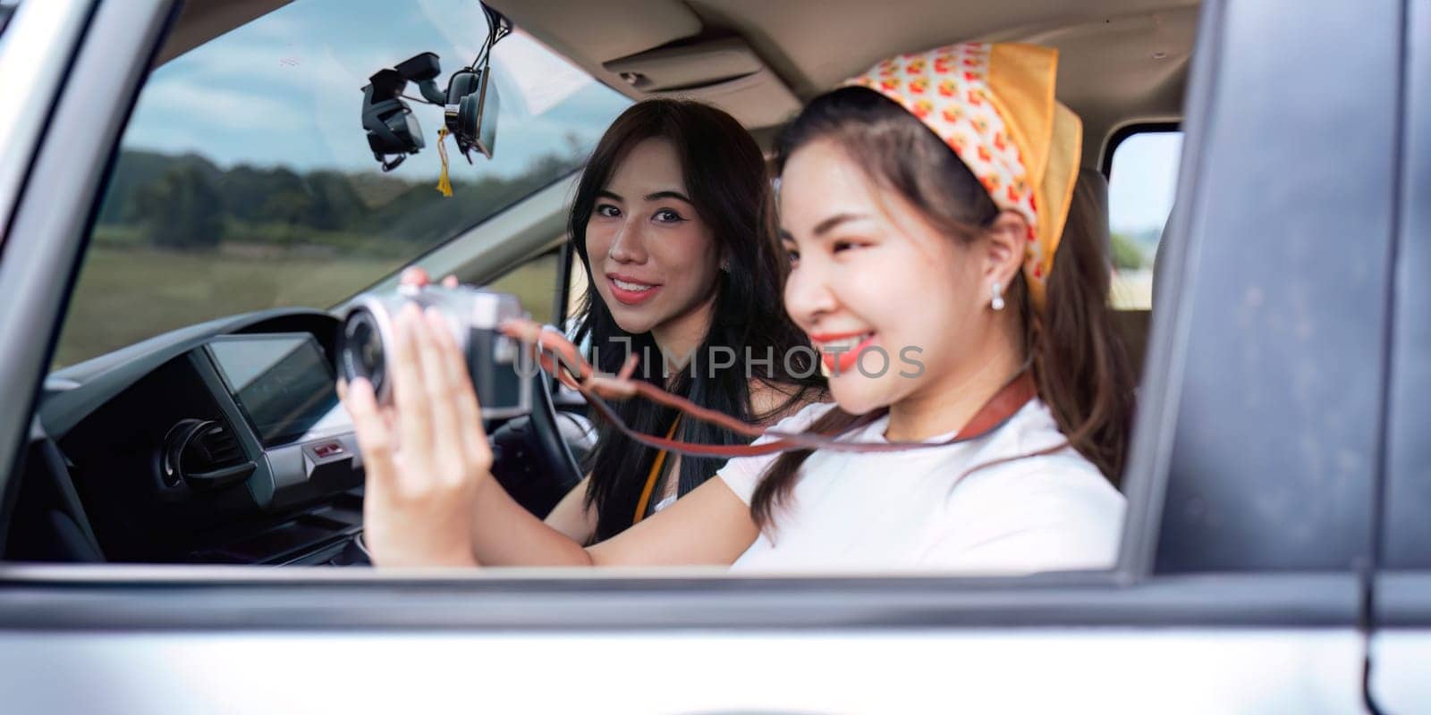 Cheerful female start smiling friends going on a trip while woman friends sticking head out of car in motion to see the view traveling.