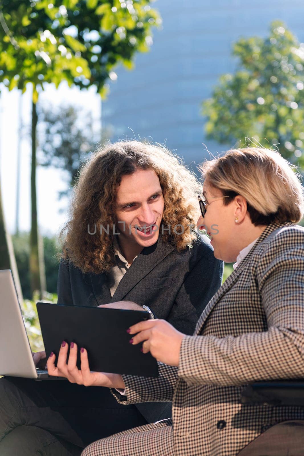 young businessman and businesswoman using wheelchair working happy outdoors with laptop and tablet, concept of diversity and urban lifestyle