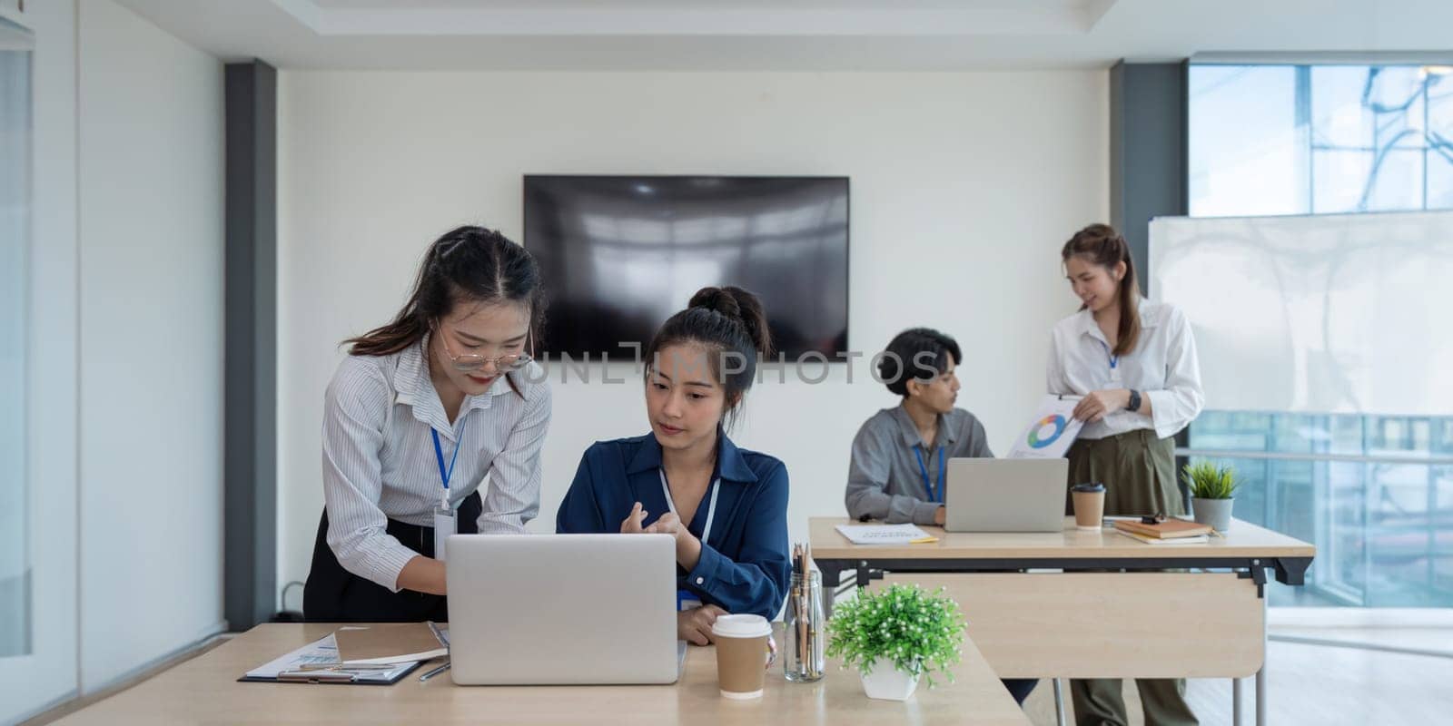 Two Business women asian looking at financial results on laptop in front of their team at the office.