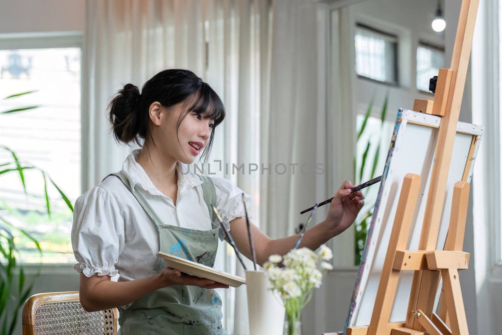 Young female artist works on abstract acrylic painting on canvas in art painting studio. by wichayada