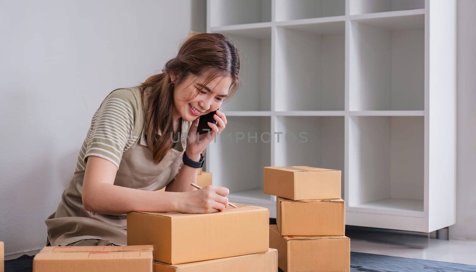 Small business entrepreneur SME freelance woman using phone call receive from customer checking product on stock at home office, online marketing packaging delivery box, SME e-commerce concept..