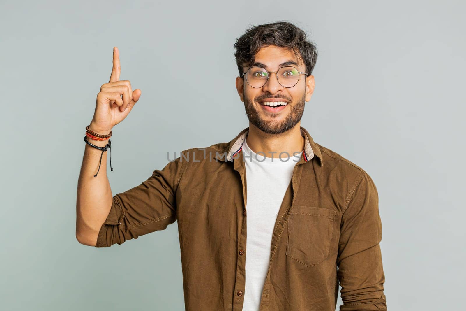 Eureka. Inspired Indian young man pointing finger up with open mouth, having good idea, plan, startup, showing inspiration motivation gesture, problem solution. Arabian guy isolated on gray background
