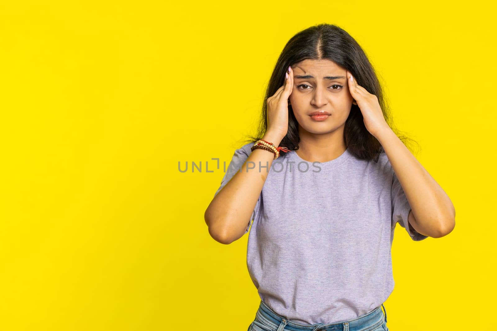 Displeased exhausted Indian Hindu woman girl rubbing temples to cure headache problem, suffering from tension, migraine, stress, grimacing in pain, high blood pressure isolated on yellow background