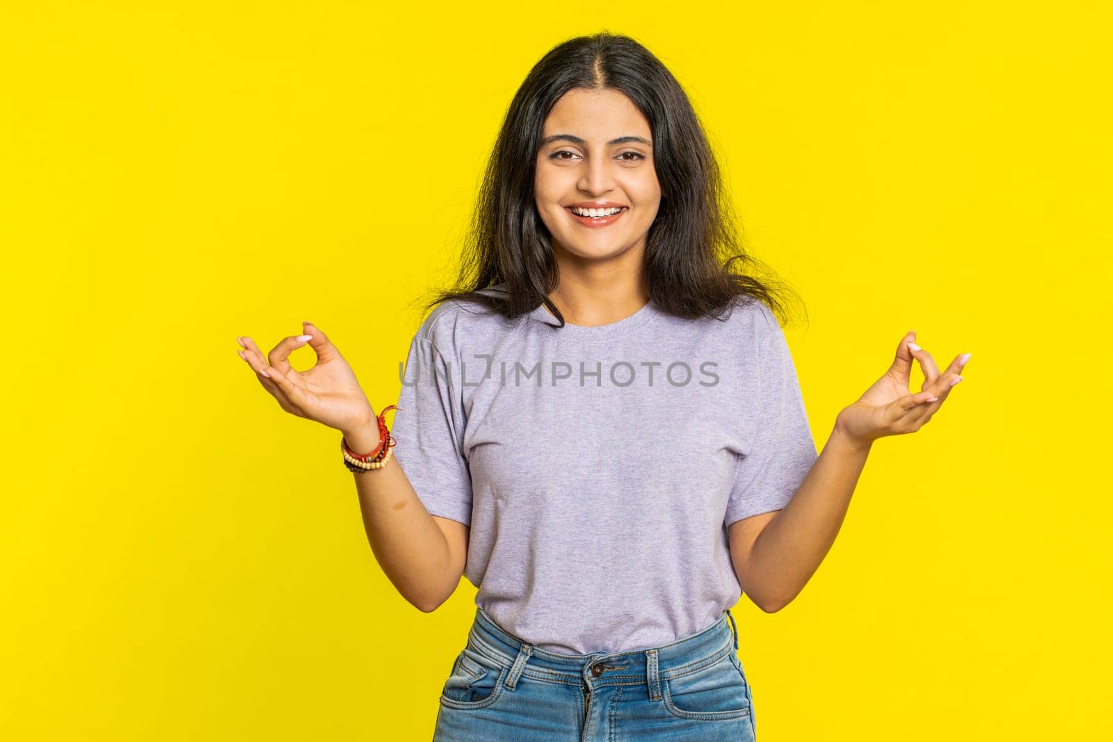 Keep calm down, relax, rest. Concentrated happy Indian woman meditating breathes deeply with mudra yoga gesture, eyes closed, peaceful mind, taking a break. Arabian Hindu girl on yellow background