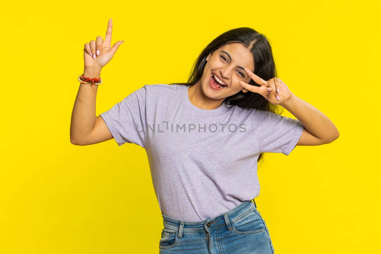 Happy smiling Indian woman listening music and dancing disco fooling around having fun expressive gesticulating hands relaxing on party making funny moves. Hindu girl isolated on yellow background