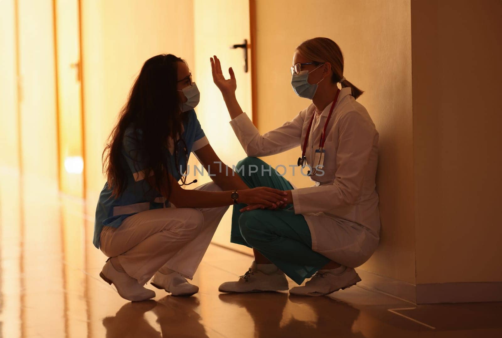 Two frustrated doctors are sitting in hospital corridor. Doctors in coronavirus pandemic concept
