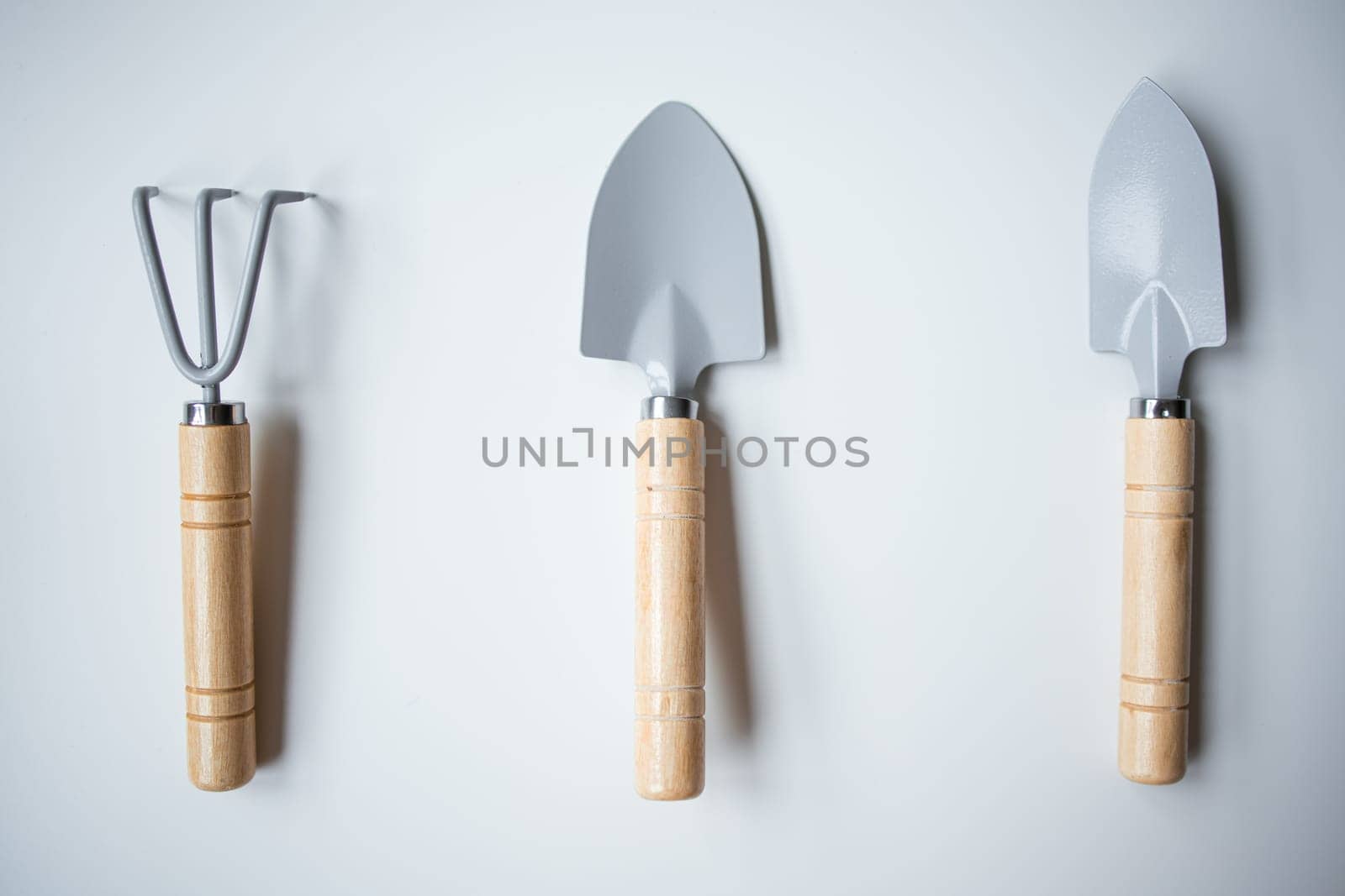 Set of three gardening tools with wooden handles on white background.