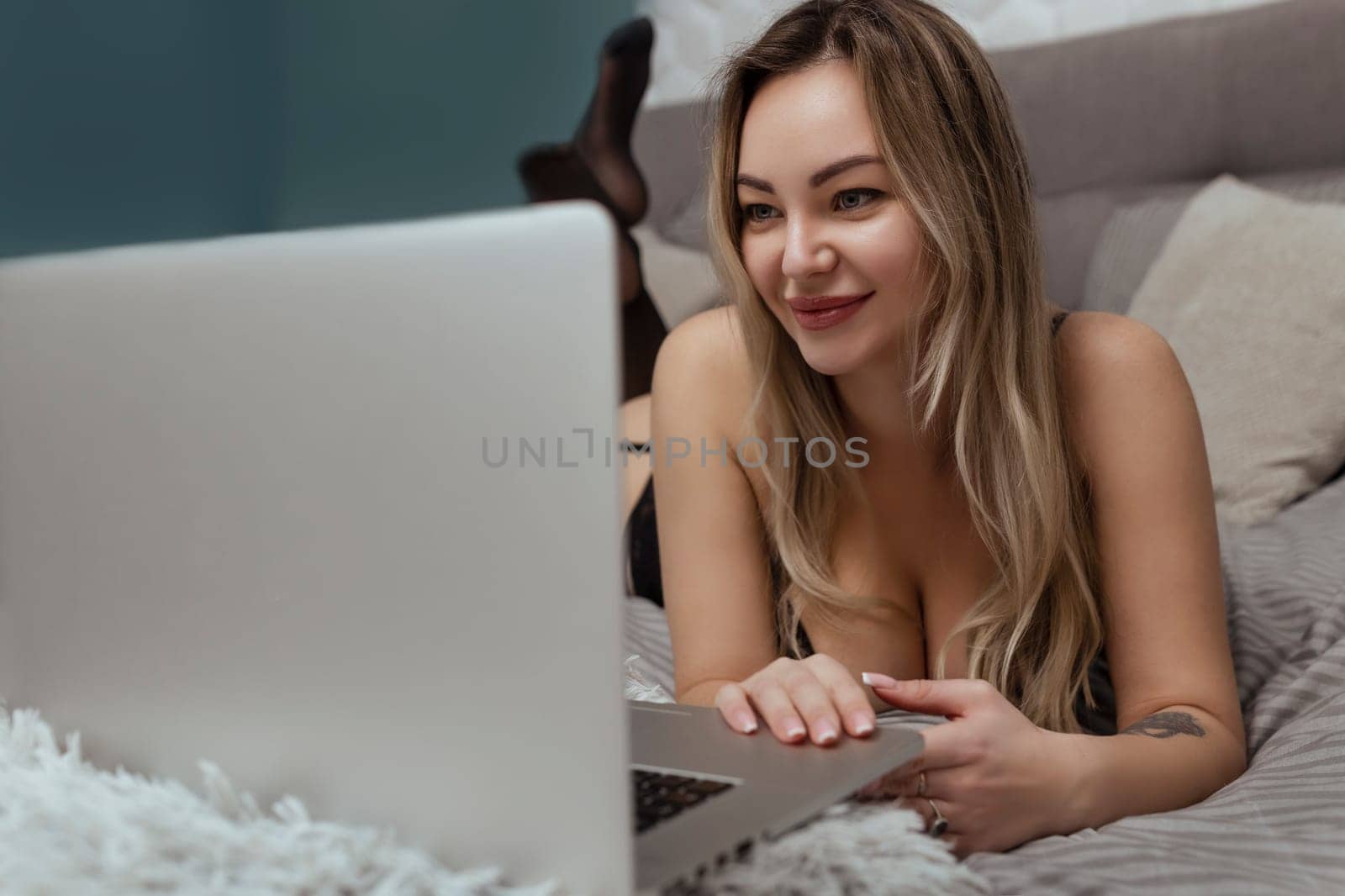 Sexy woman in black lingerie lies on the bed and uses a laptop. Sex model concept on webcam and dating site.