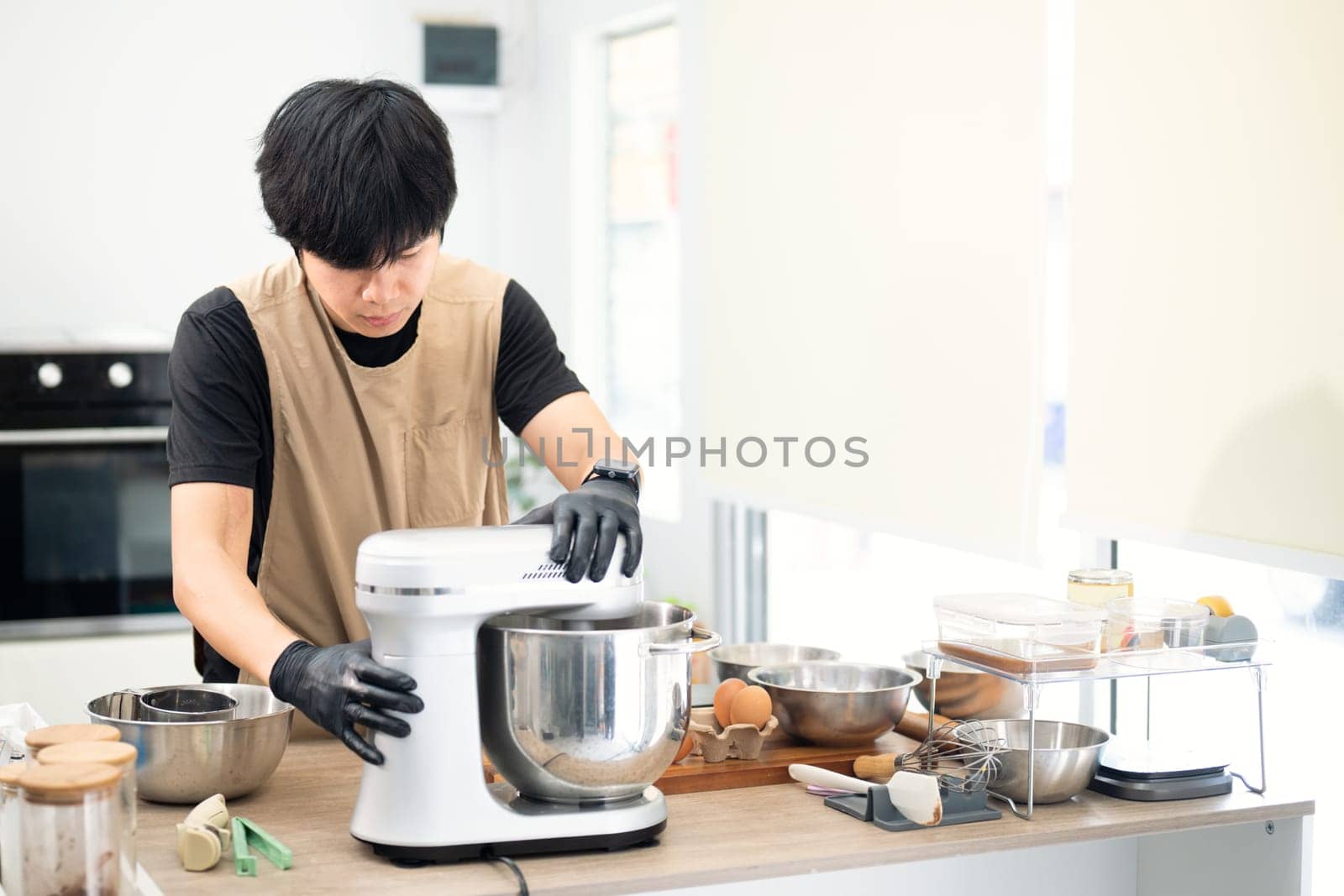 Asian male baker using a stand mixer to prepare cookie dough.