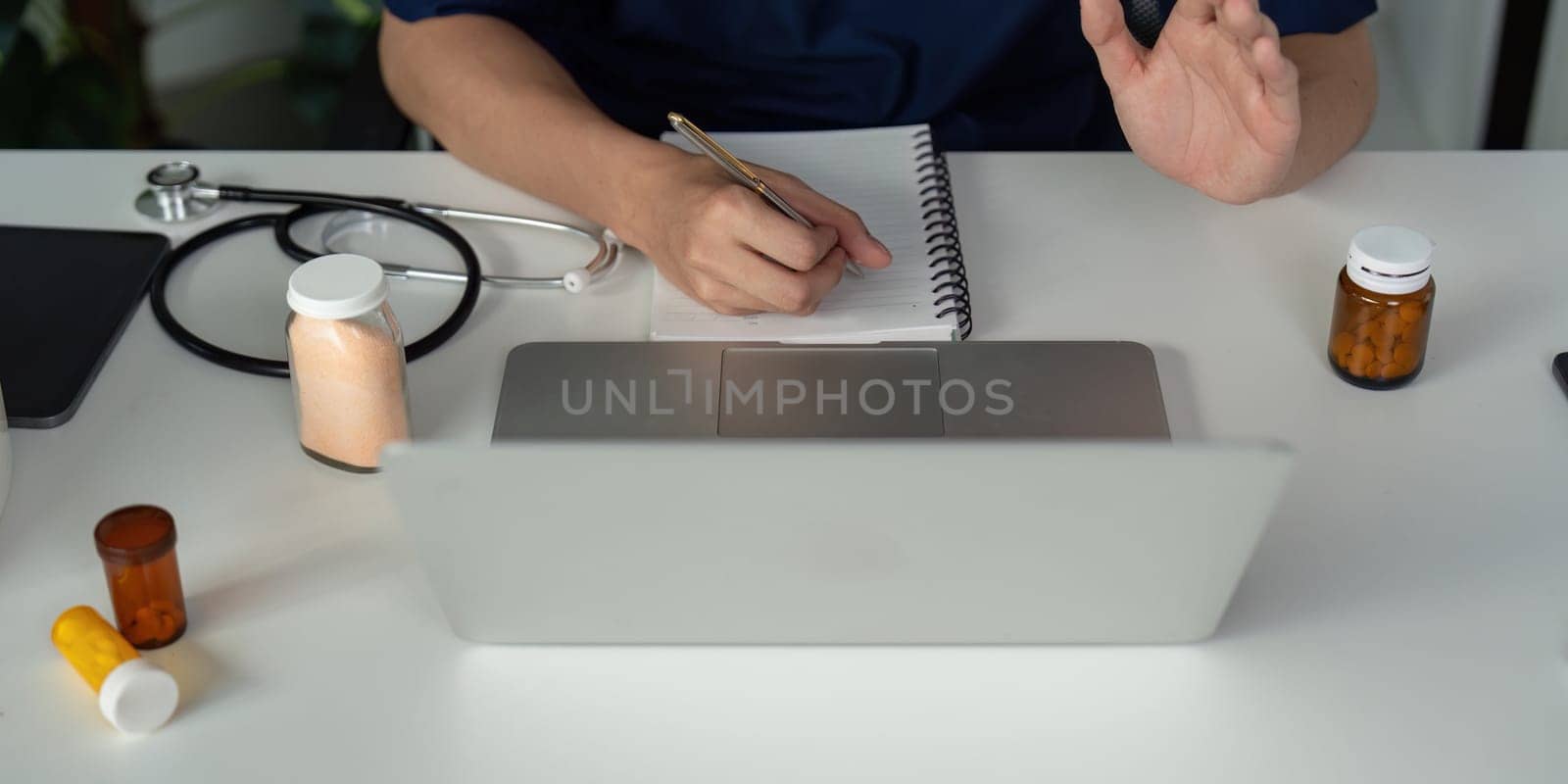 A focused medical student writes notes and analyzes medication bottles during an online study session, showcasing dedication to healthcare.