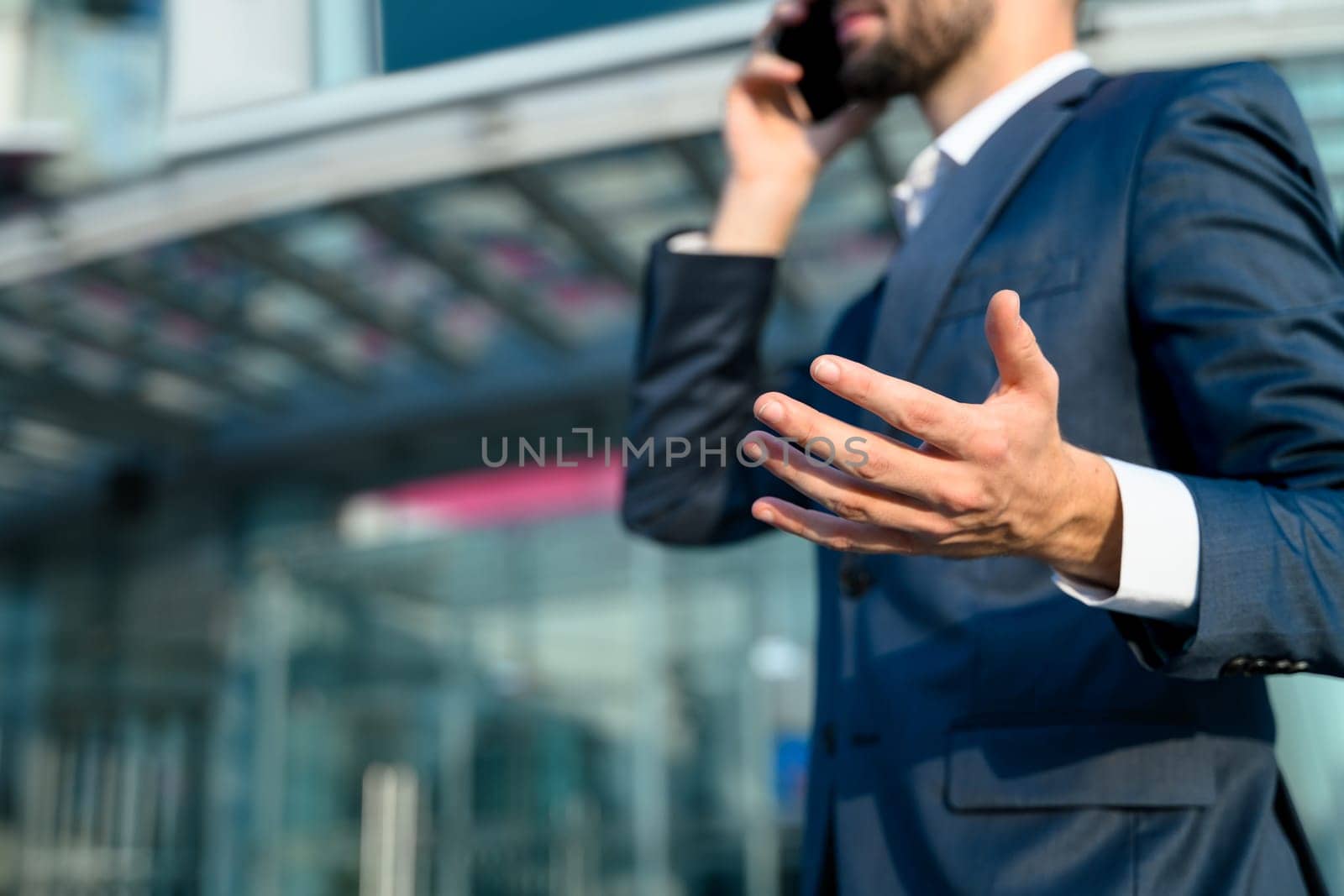 Professional businessman in a navy blue suit talking on mobile phone outside a modern office building.