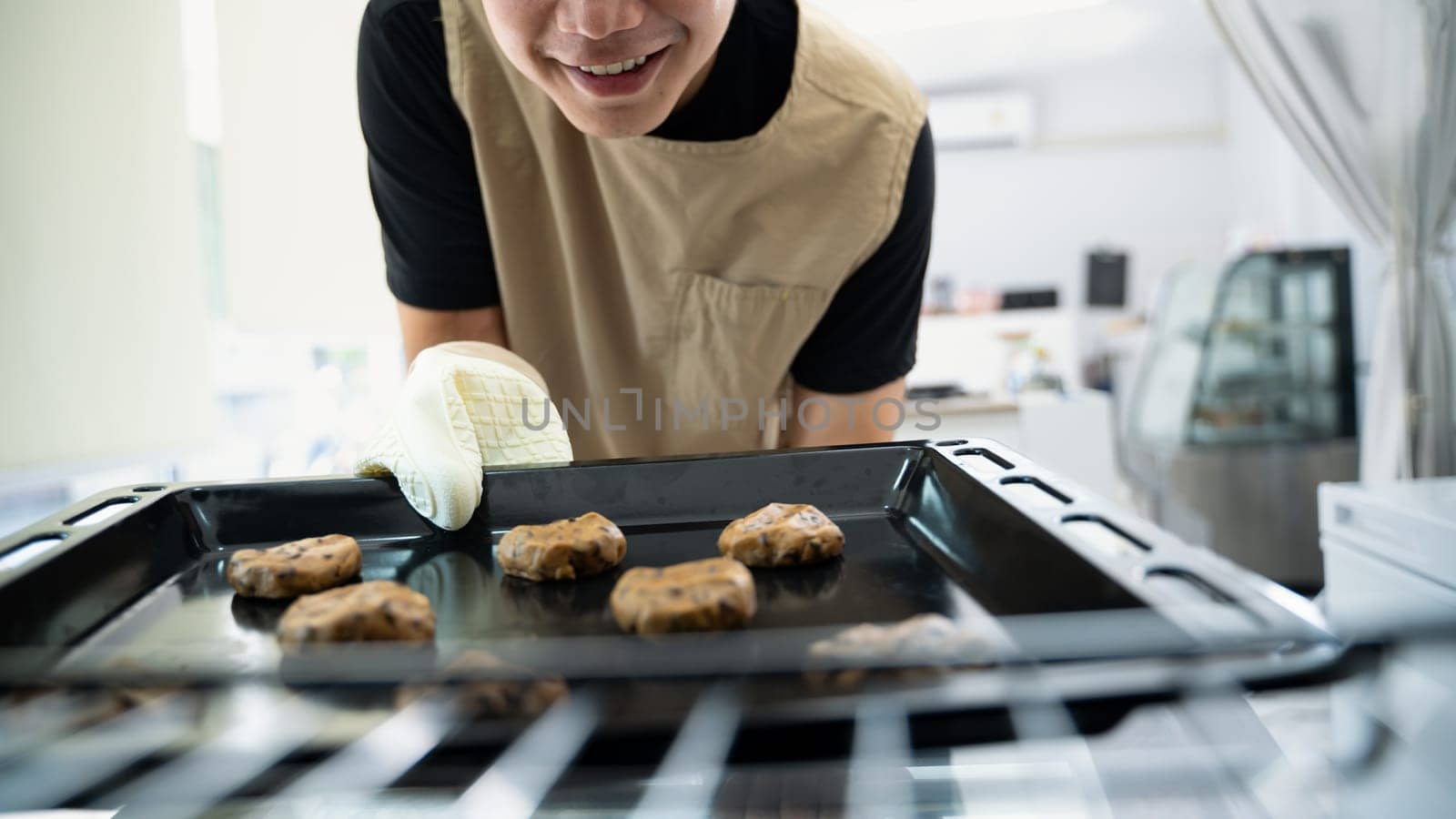 Cheerful male baker a tray of chocolate chip cookie dough into the oven.
