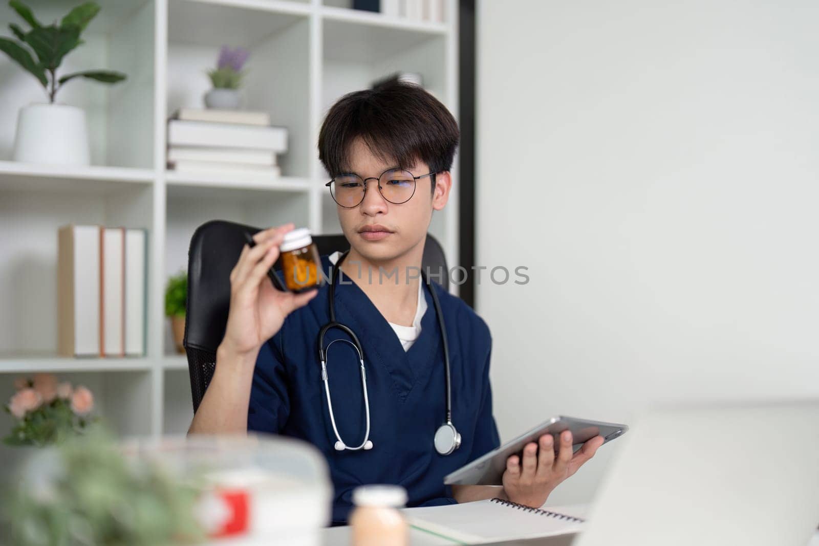 A diligent medical student in scrubs examines a medication bottle while using a tablet, highlighting the importance of study and medication management.