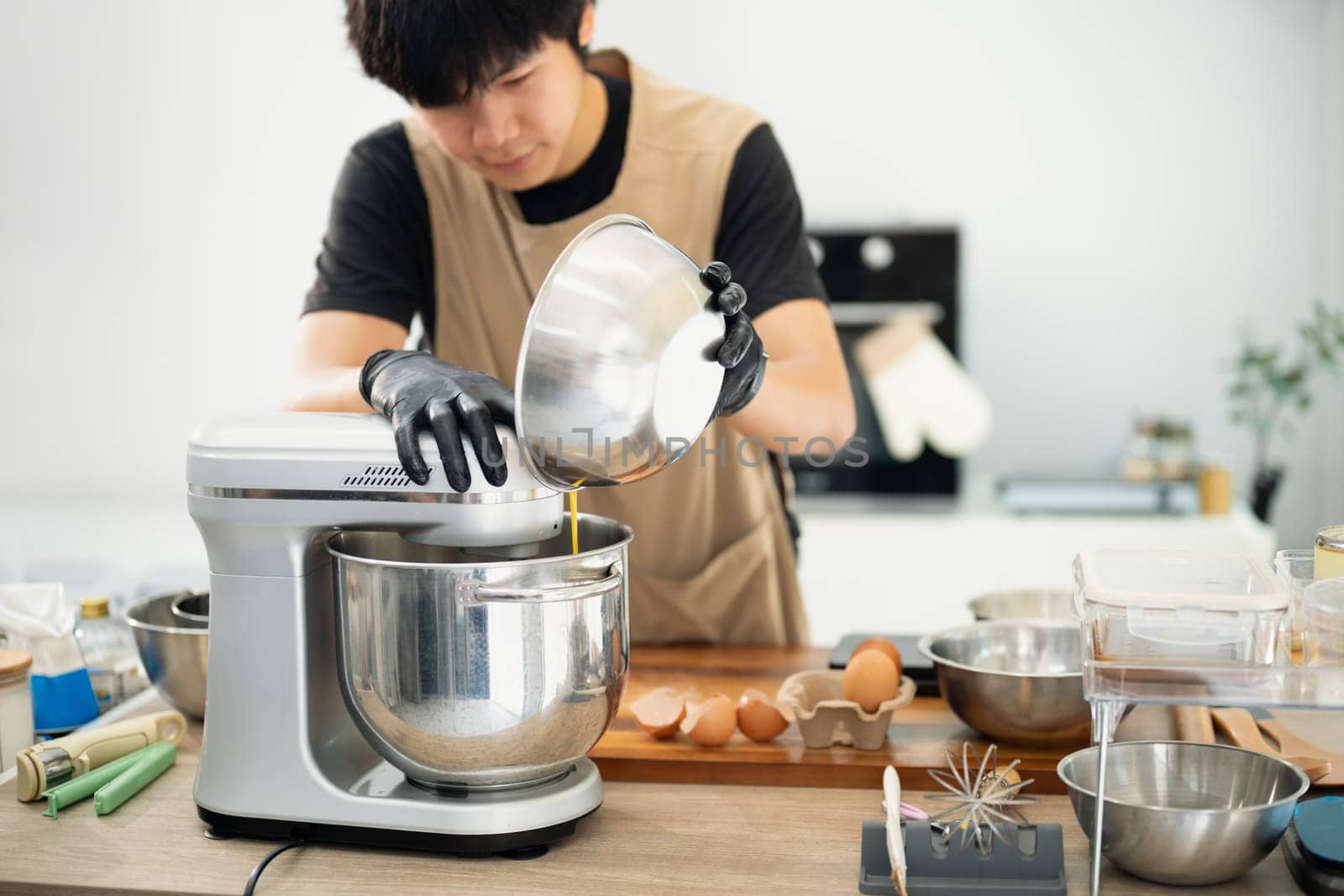 Male baker adding ingredients to a stand mixer for cookie dough.