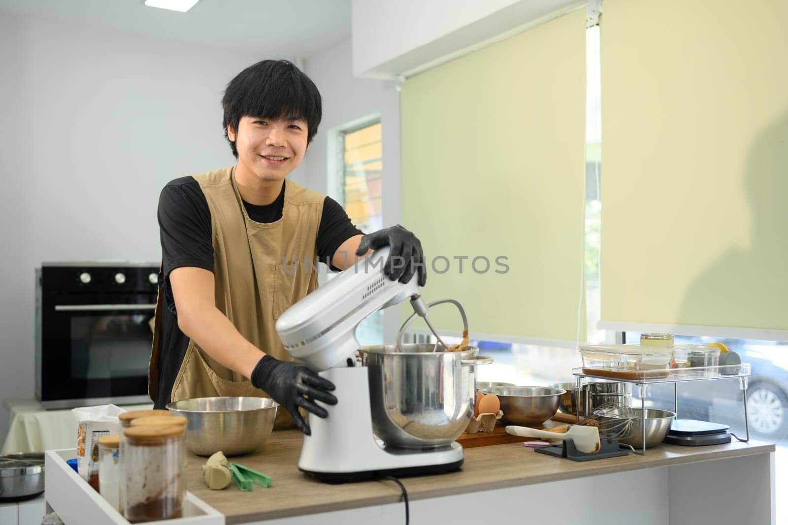 Smiling young baker preparing cookie dough and using a stand mixer in a kitchen.