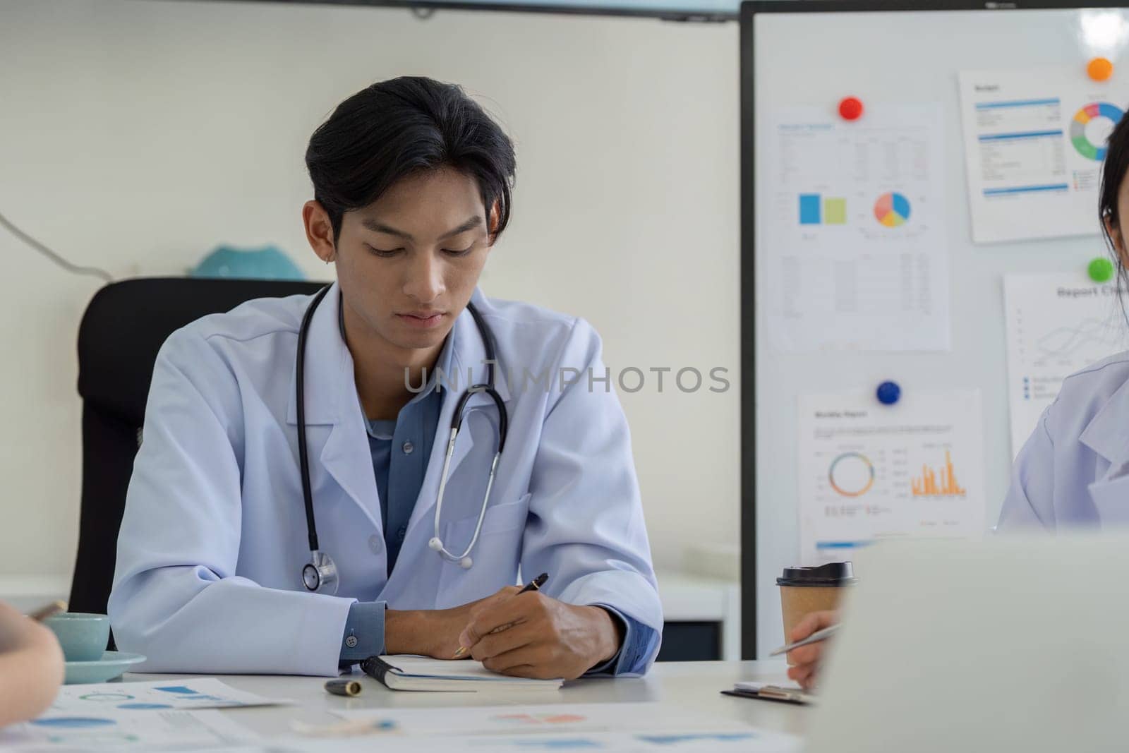 A doctor actively participates in a meeting, taking notes while discussing healthcare strategies and data analysis with the team.