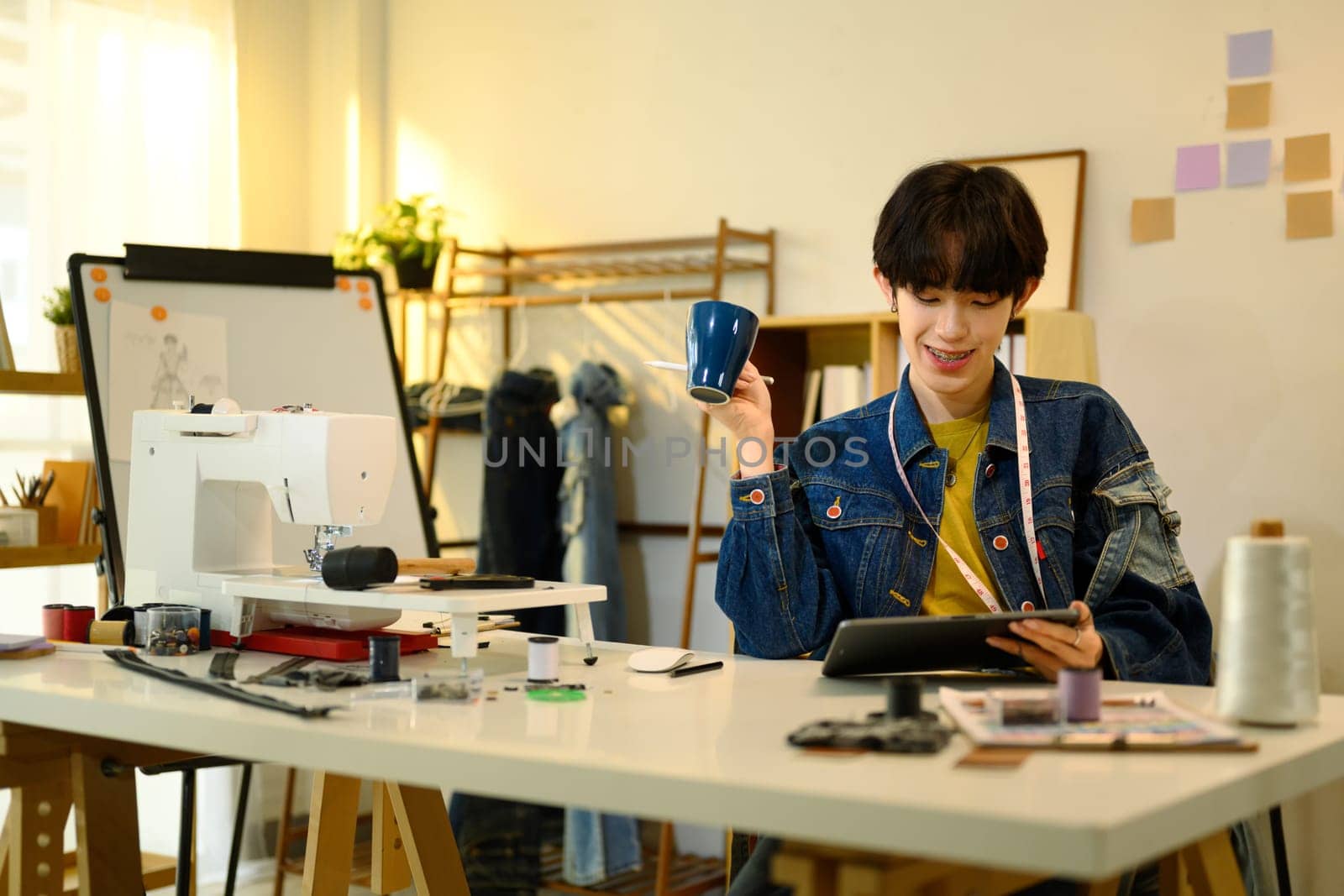 Designer holding a cup of coffee and using digital tablet in a creative studio.